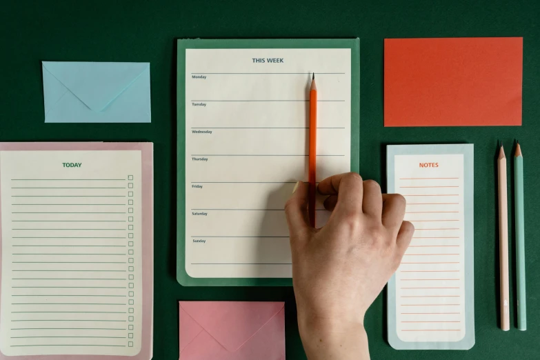 a person writing on a notepad with a pencil, inspired by Wes Anderson, trending on unsplash, green and orange theme, paper border, various sizes, female calendar