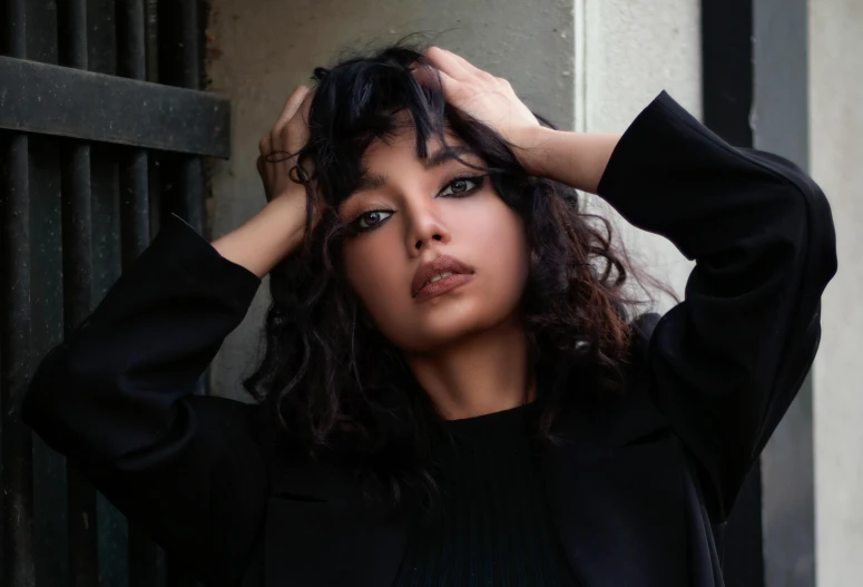 a woman leaning against a wall with her hands on her head, an album cover, trending on pexels, hurufiyya, wearing a black jacket, curly middle part haircut, beautiful asian woman, asher duran