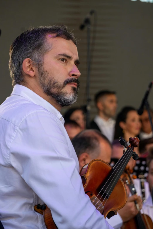 a man in a white shirt holding a violin, by Alejandro Obregón, reddit, audience in the background, profile image, conductor, close-up photo
