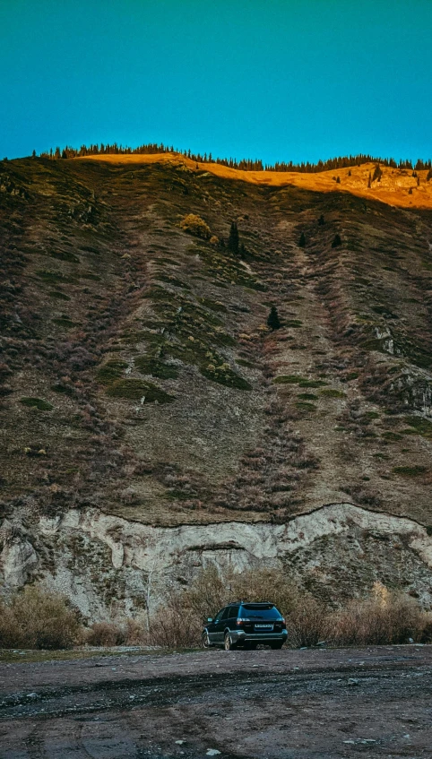 a car parked on the side of a dirt road, an album cover, by Elsa Bleda, pexels contest winner, figuration libre, geological strata, hillside, evening sun, drone photo