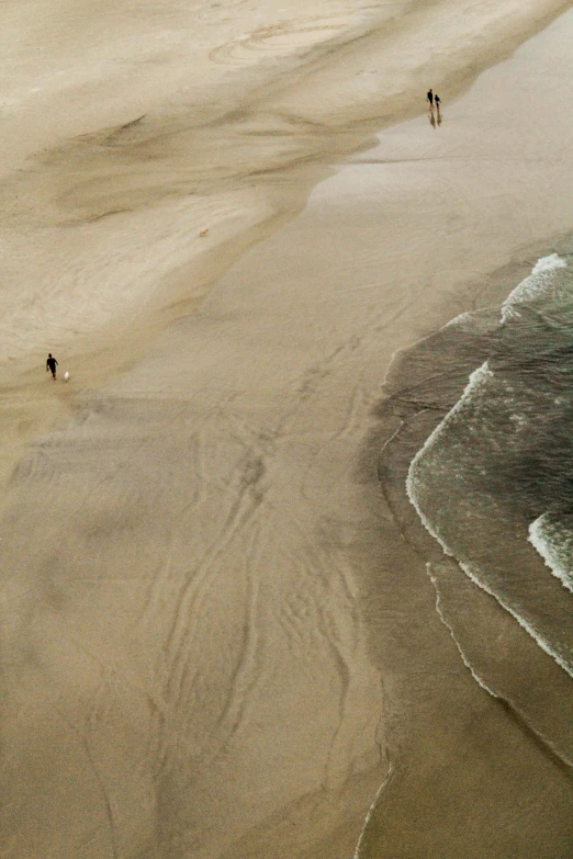 a group of people standing on top of a sandy beach, bird view, lone person in the distance, walking down, the ocean