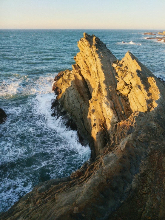 a man standing on top of a cliff next to the ocean, inspired by Juan de Flandes, pexels contest winner, renaissance, sharp spiky rocks, late afternoon light, aerial shot from the drone, today\'s featured photograph 4k