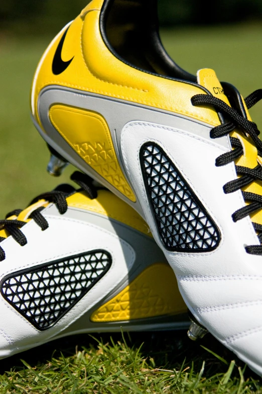 a pair of soccer shoes sitting on top of a green field, yellow and black trim, features intricate detail, up close shot, whites