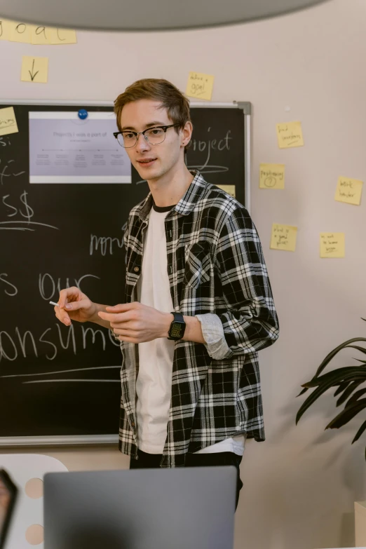 a man standing in front of a blackboard with writing on it, a picture, by Jacob Toorenvliet, pexels contest winner, wearing business casual dress, non binary model, flannel, around 1 9 years old