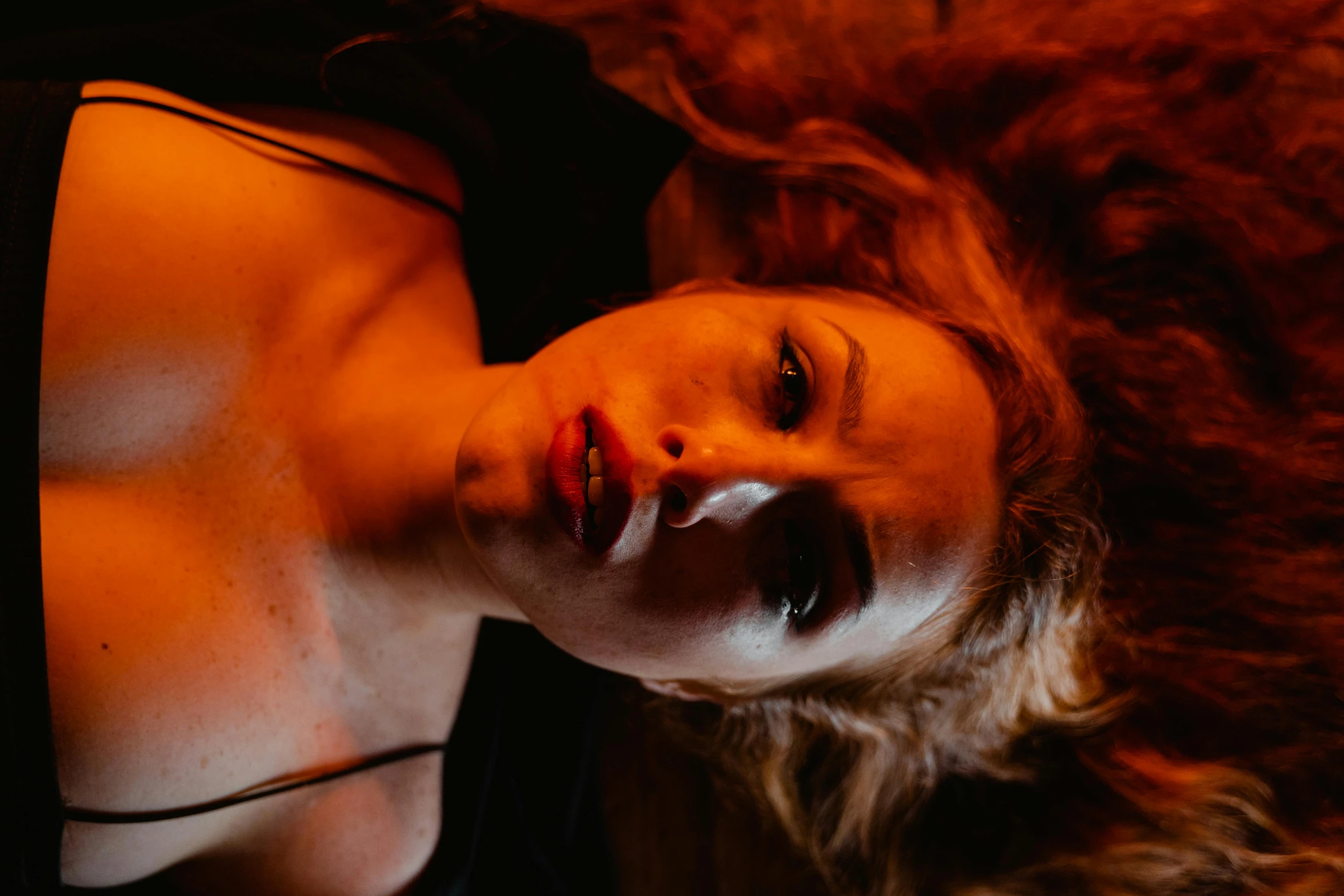 a woman laying down with her eyes closed, inspired by Elsa Bleda, renaissance, thick red lips, warm orange lighting, film still from horror movie, looking up at the camera