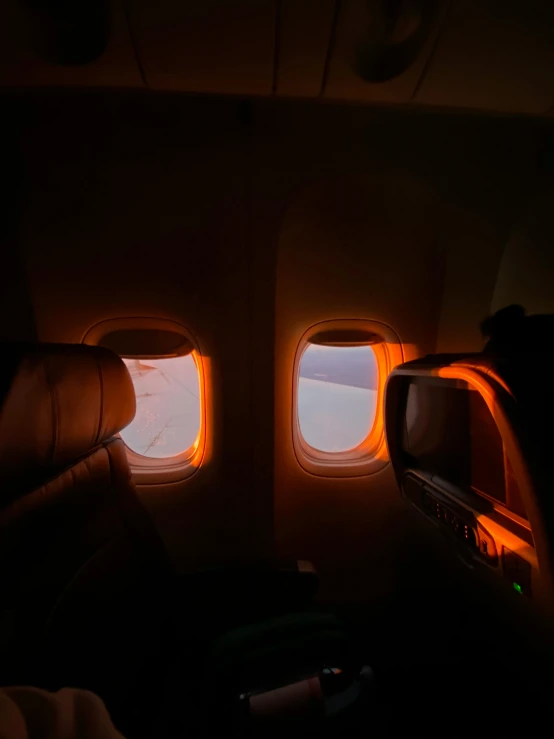 a person sitting in an airplane looking out the window, a picture, light and space, orange lights, very dark with green lights, oled lights in corners, sunlight pouring through window
