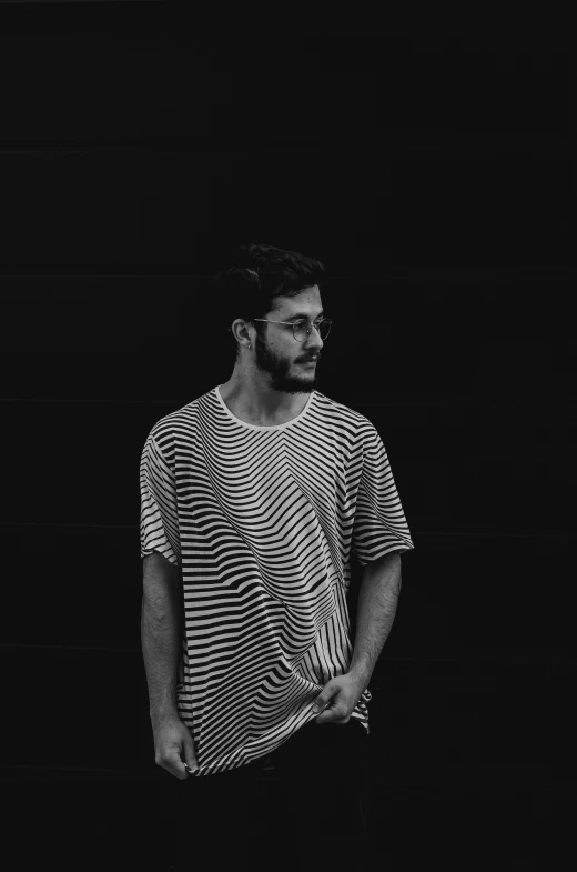 a man standing in front of a black wall, a black and white photo, inspired by Alexis Grimou, unsplash, serial art, wearing stripe shirt, gal yosef, chillwave, slightly pixelated