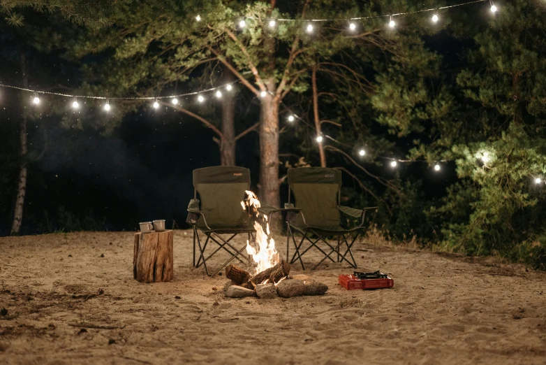 a couple of lawn chairs sitting next to a fire, by Jessie Algie, unsplash contest winner, fairy lights, camping, 3 / 4 wide shot, beach setting