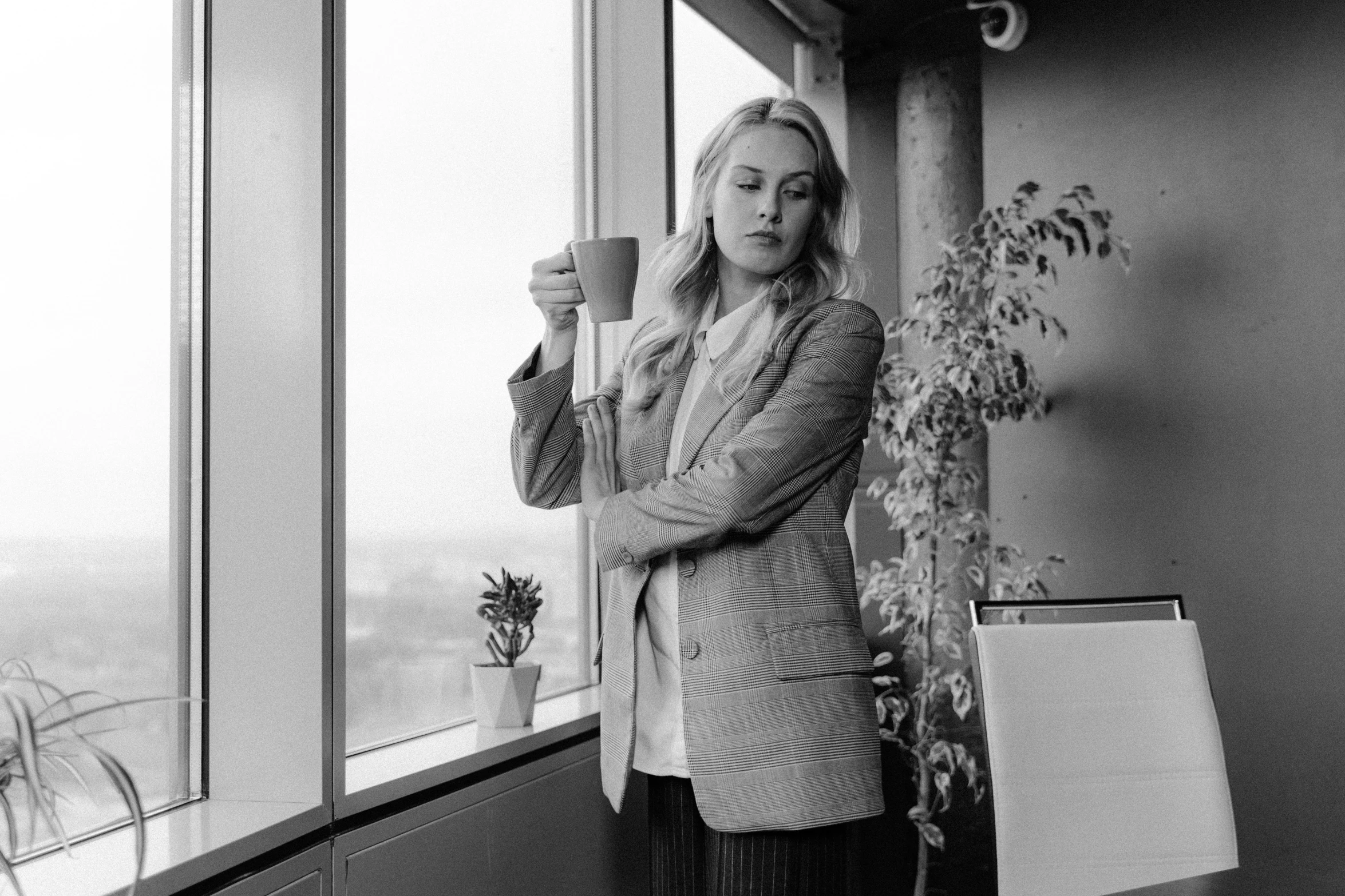 a black and white photo of a woman holding a cup, by Emma Andijewska, business attire, blonde swedish woman, big windows, concerned