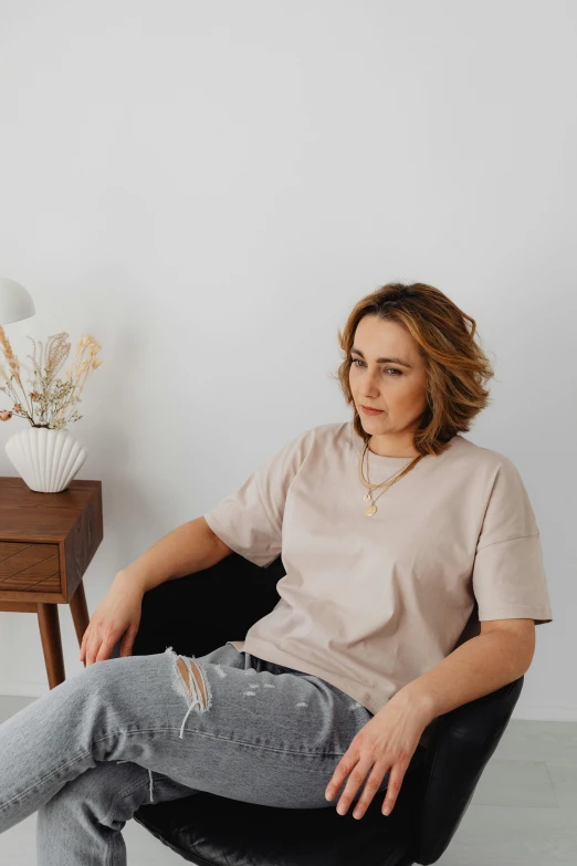 a woman sitting in a chair in a room, inspired by Ilka Gedő, trending on pexels, happening, wear's beige shirt, wearing a t-shirt, neutral background, thicc