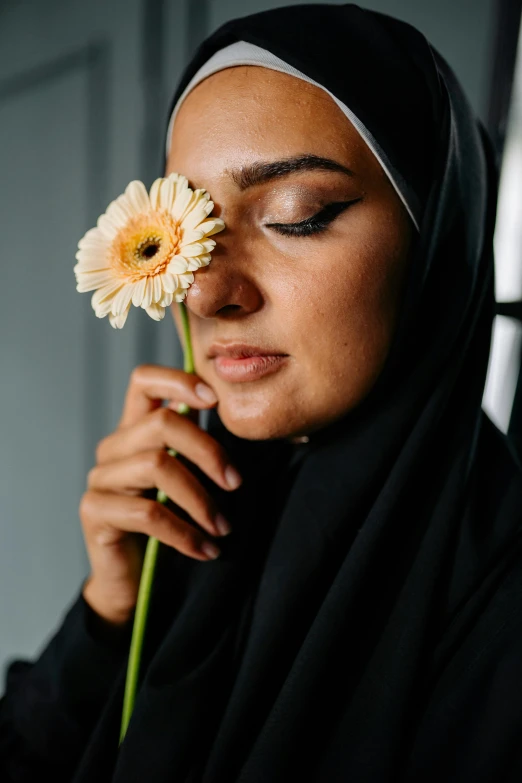 a woman in a black hijab holding a flower, inspired by Maryam Hashemi, trending on unsplash, contemplative, light skin, indoor picture, mixed-race woman