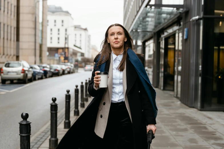 a woman walking down a street holding a cup of coffee, by Emma Andijewska, pexels contest winner, trench coat and suit, ukrainian, office clothes, thumbnail