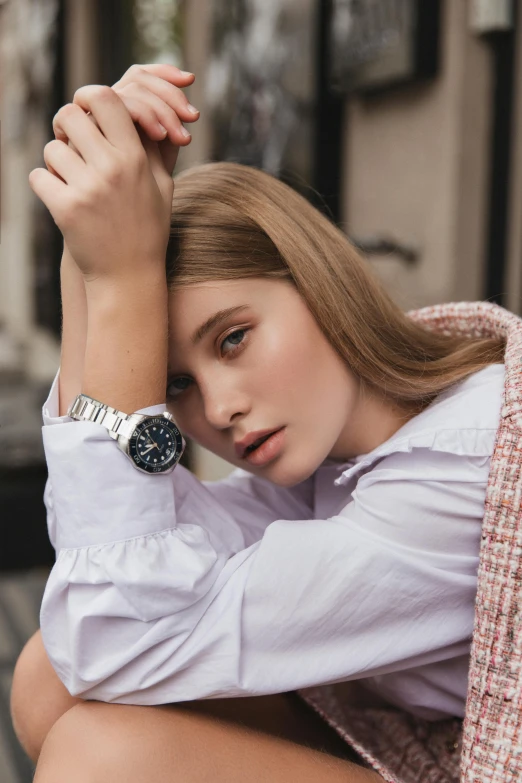 a woman sitting on the ground with a watch on her wrist, inspired by Emma Andijewska, titanium white, model face, 40mm, woman astronaut