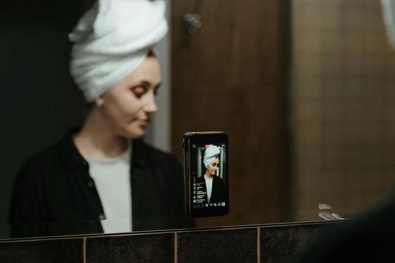 a woman taking a picture of herself in the mirror, a hologram, trending on pexels, hyperrealism, wearing a turban, wearing black robe, taken with sony alpha 9, photoshoot for skincare brand