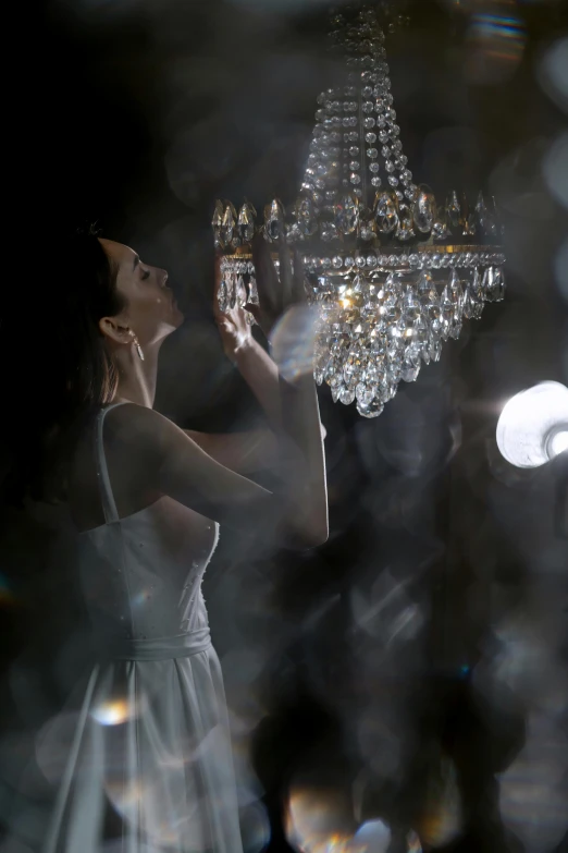 a woman in a white dress standing in front of a chandelier, inspired by Jerry Schatzberg, light and space, ;cinematic lighting, product lighting, crystal lighting, ethereal lighting - h 640