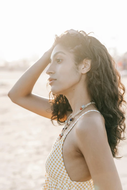 a woman standing on top of a sandy beach, trending on pexels, renaissance, long wild black curly hair, focused on her neck, retro and ethereal, halfbody headshot