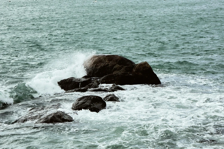 a large rock in the middle of a body of water, unsplash, waves crashing at rocks, midday photograph, set photo