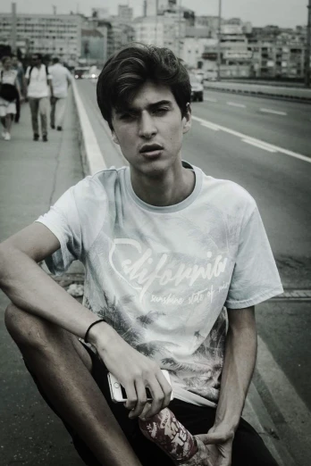 a young man sitting on top of a skateboard, a black and white photo, by Tamas Galambos, wearing a tie-dye t-shirt, wears a light grey crown, on sidewalk, androgynous person
