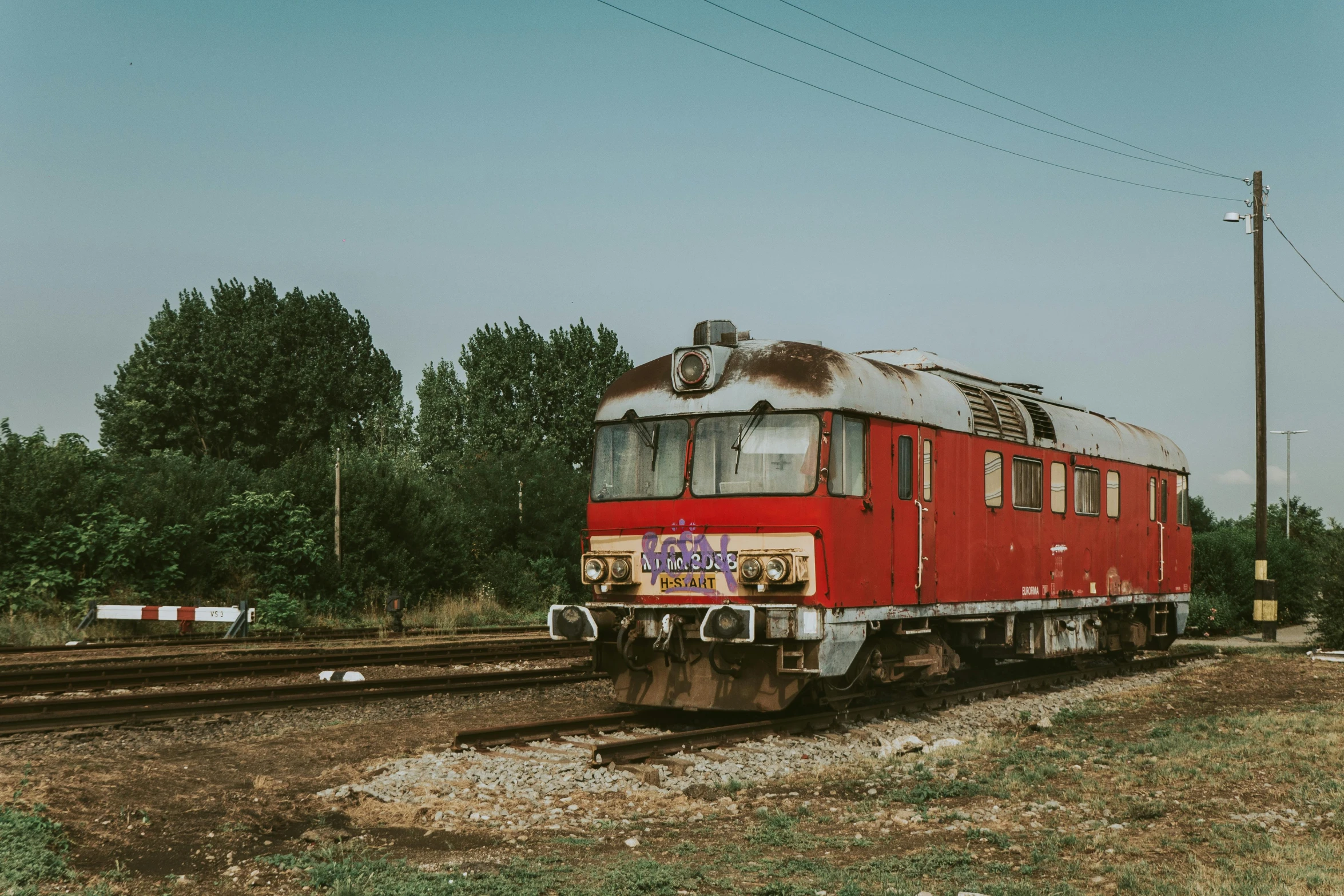 a red train traveling down train tracks next to a forest, a portrait, unsplash contest winner, graffiti, soviet yard, faded and dusty, 🚿🗝📝