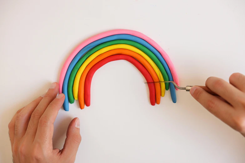 a person using a pair of scissors to cut a rainbow, by Rachel Reckitt, made out of clay, edible, rounded lines, looking towards camera