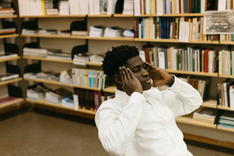 a man sitting in front of a bookshelf talking on a cell phone, by Stokely Webster, pexels contest winner, academic art, curls on top of his head, jaylen brown, doing an elegant pose, sitting in the classroom