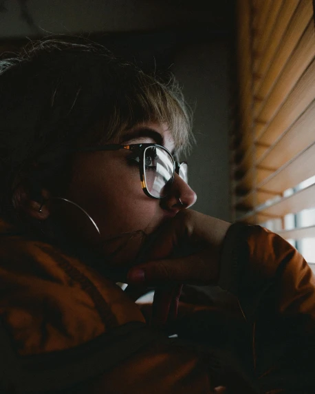 a close up of a person sitting in front of a window, inspired by Elsa Bleda, trending on pexels, wearing goggles, queer woman, sleepy expression, late evening