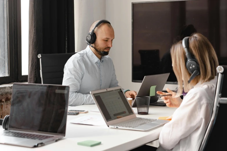 a couple of people sitting at a table with laptops, pexels contest winner, hurufiyya, working in a call center, headphones on his head, lachlan bailey, cubical meeting room office