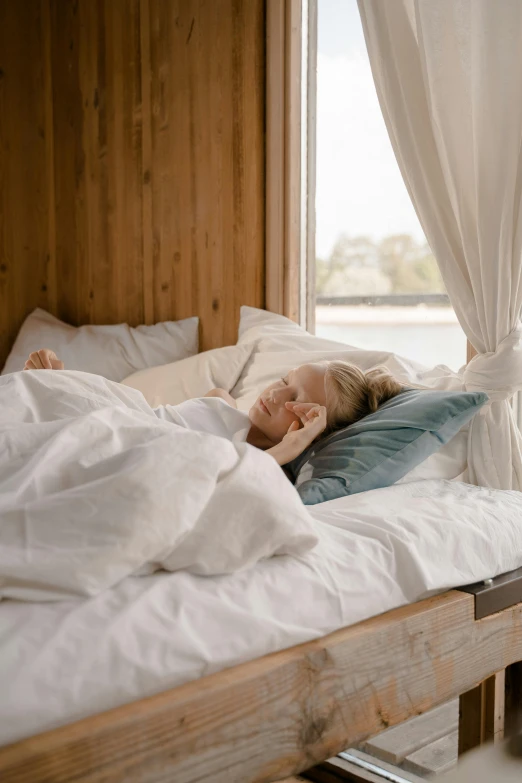 a woman laying on top of a bed next to a window, pexels contest winner, happy cozy feelings, profile image, scandinavian, fully covered in drapes