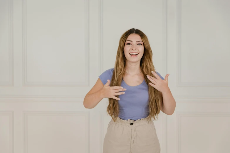 a beautiful young woman standing in front of a white wall, trending on pexels, antipodeans, gestures, animation, wearing a cute top, excited