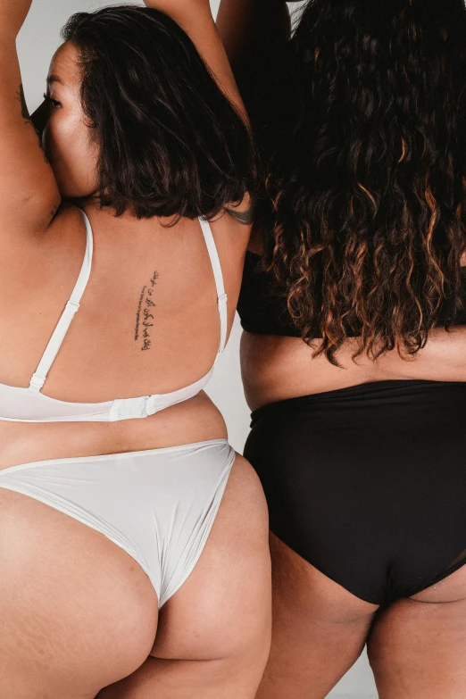 a couple of women standing next to each other, a tattoo, by Jessie Alexandra Dick, trending on unsplash, curvy accentuated booty, product introduction photo, bra strap, white and black