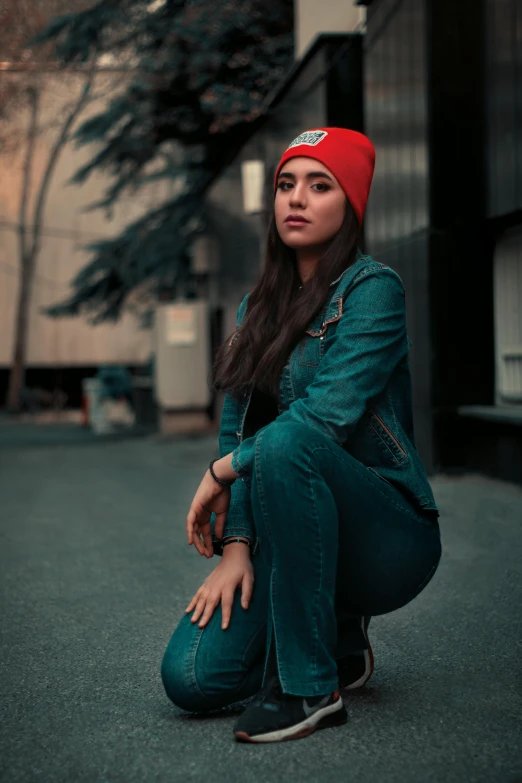 a woman sitting on the ground wearing a red beanie, inspired by Elsa Bleda, trending on pexels, teal suit, women full body, profile pic, wearing a jeans jackets