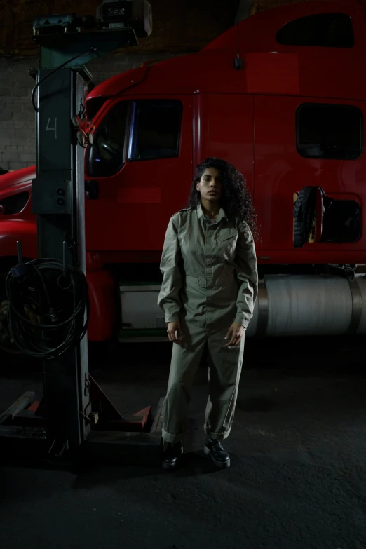 a woman standing in front of a red truck, reflective suit, standing in a dimly lit room, mechanics, ( ( theatrical ) )