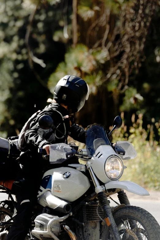 a man riding on the back of a motorcycle down a road, wearing her helmet, profile image, amongst foliage, bmw