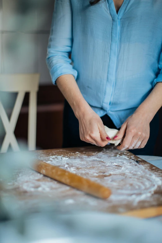 a woman in a blue shirt preparing food on a table, trending on unsplash, square, pastry, carving, covered in white flour