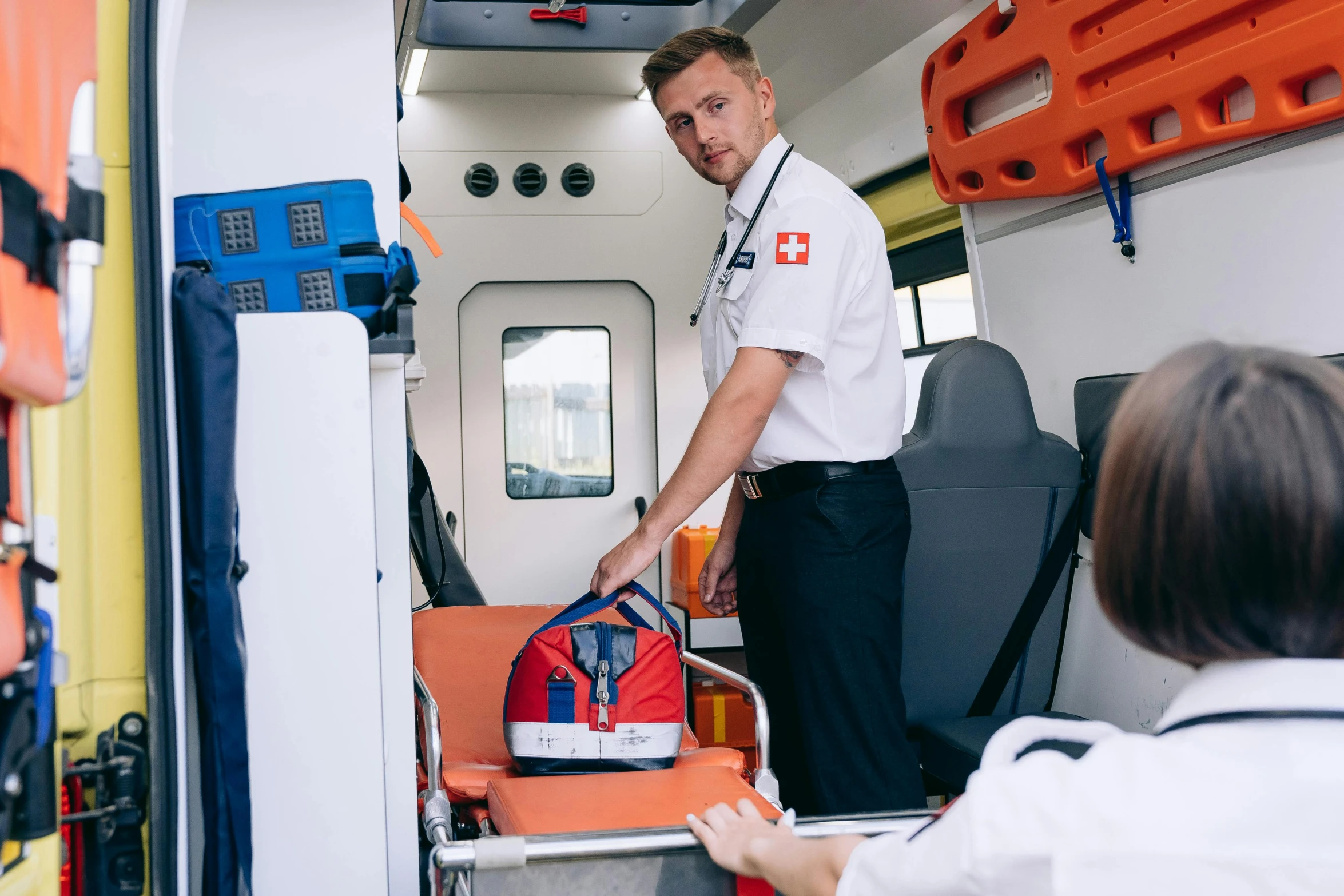 a man standing next to a woman in an ambulance, by Julia Pishtar, pexels, happening, white and orange breastplate, with a backpack, avatar image, medical supplies