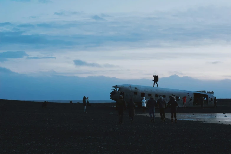 a group of people standing around an airplane on a beach, by Jesper Knudsen, pexels contest winner, visual art, mutants roaming in the evening, crashed in the ground, hd footage, iceland