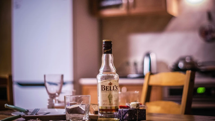 a bottle of alcohol sitting on top of a wooden table, inspired by Bedwyr Williams, pexels contest winner, bells, on kitchen table, belle, short dof