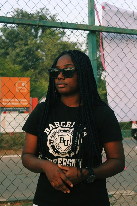 a woman with dreadlocks standing in front of a fence, an album cover, by Daarken, pexels contest winner, black arts movement, wearing a black tshirt, wearing shades, college, profile image