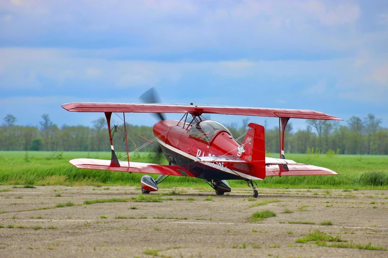 a small red airplane sitting on top of an airport tarmac, by Arnie Swekel, pexels contest winner, biplanes flying, tomcat replica, spring season, minn