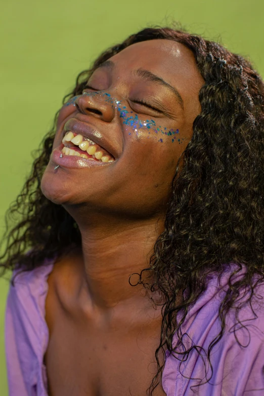 a woman with blue paint on her face laughing, purple sparkles, dark skinned, summertime, trending photo