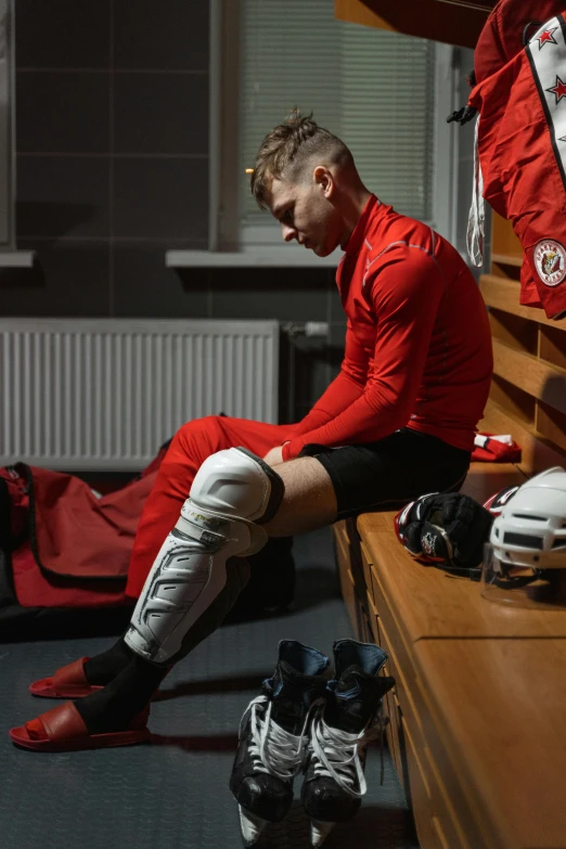 a man sitting on a bench in a locker, inspired by Kaff Gerrard, wearing a red captain's uniform, compression, lpoty, knee pads