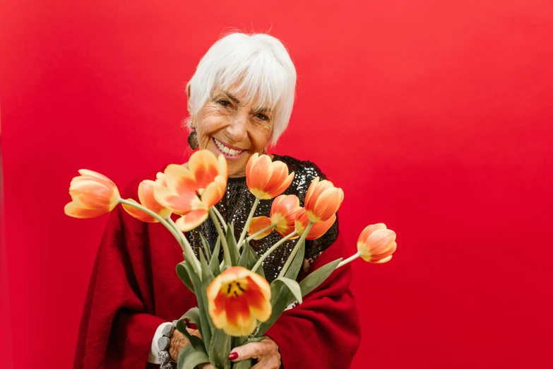 a woman holding a bouquet of flowers in front of a red wall, pexels contest winner, silver haired, tulips, 15081959 21121991 01012000 4k, smiling playfully