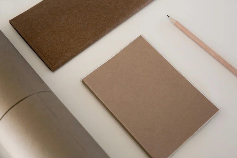 a brown notebook sitting on top of a table next to a pencil, an album cover, inspired by Rachel Whiteread, unsplash, visual art, white box, felt, made of cardboard, taupe