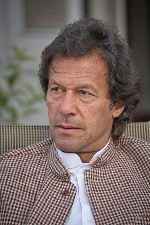 a close up of a person sitting on a couch, a picture, dau-al-set, wearing green suit, light stubble with red shirt, mogul khan, wikimedia commons