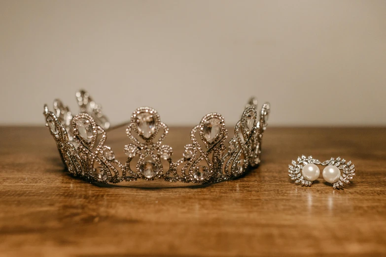 a crown sitting on top of a wooden table, by Emma Andijewska, pexels contest winner, silver earring, fan favorite, tiffany dover, decoration