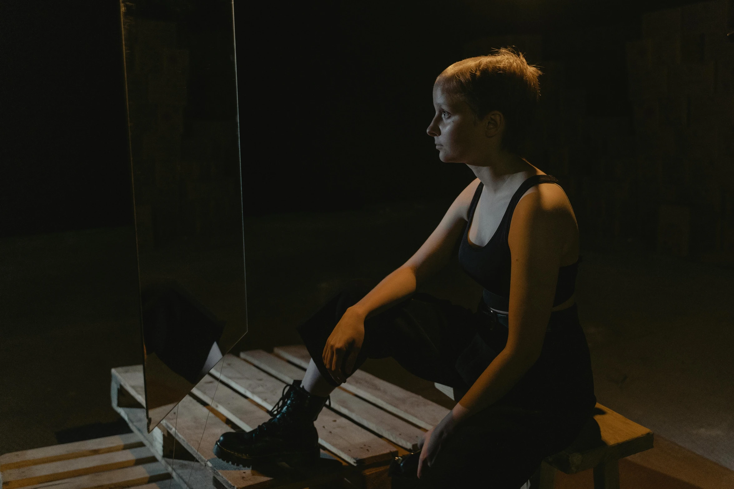 a woman sitting on top of a wooden bench, a portrait, inspired by Elsa Bleda, pexels contest winner, realism, in a pitch black room, looking in a mirror, still from a music video, in a warehouse