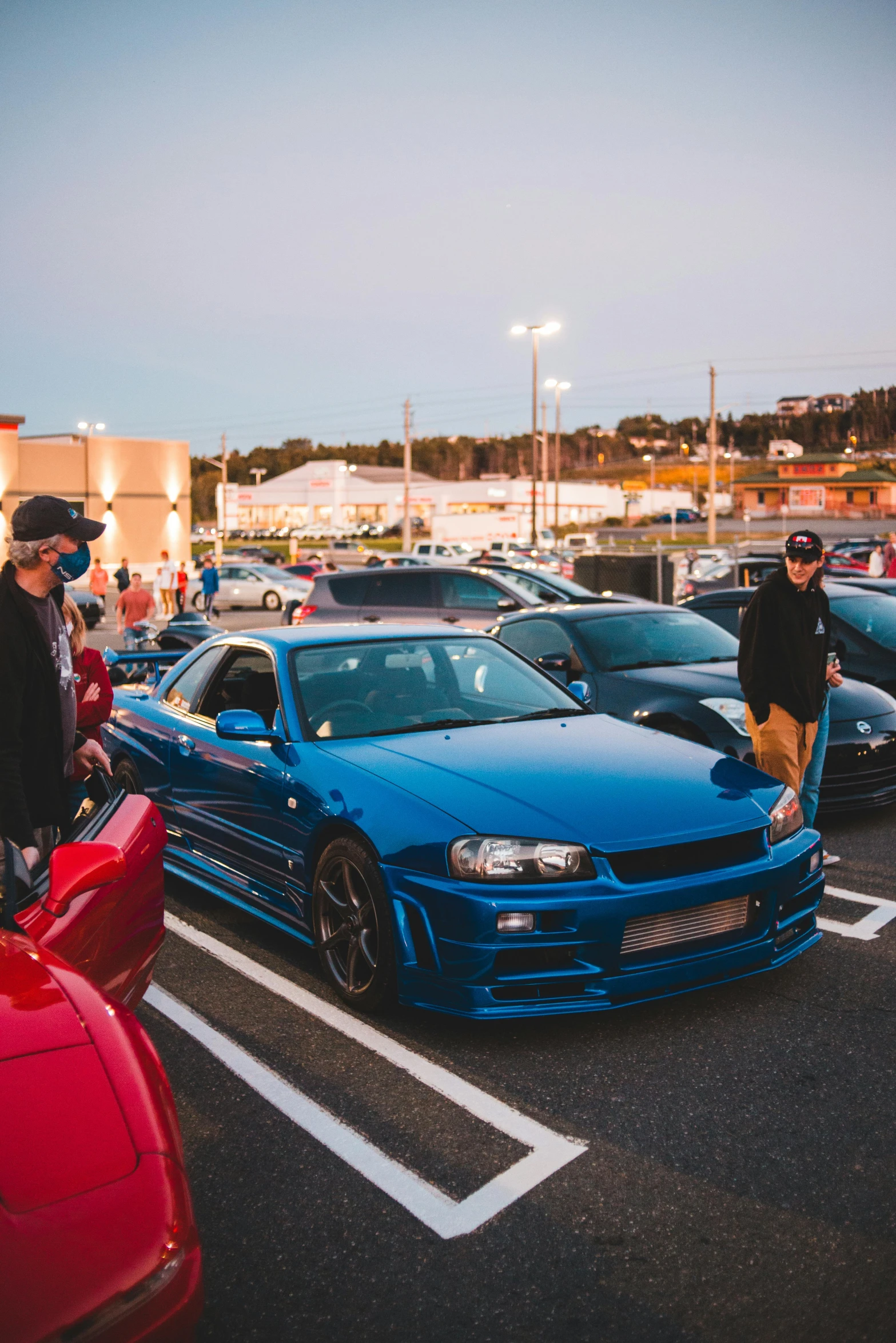 a group of cars parked next to each other in a parking lot, by Tom Bonson, pexels contest winner, in a modified nissan skyline r34, people enjoying the show, dressed in blue, mutants roaming in the evening