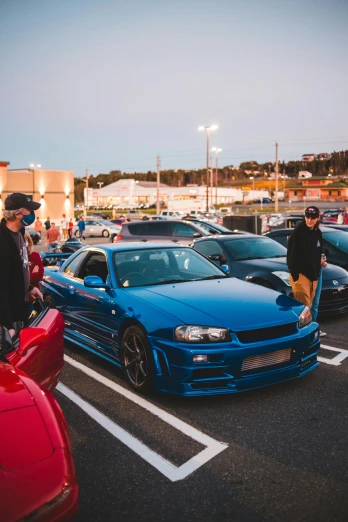 a group of cars parked next to each other in a parking lot, by Tom Bonson, pexels contest winner, in a modified nissan skyline r34, people enjoying the show, dressed in blue, mutants roaming in the evening