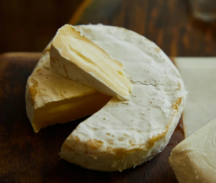 a piece of cheese sitting on top of a wooden cutting board, by Jessie Algie, renaissance, fan favorite, white, medium angle, round format