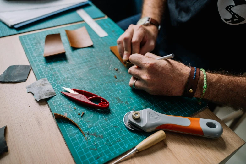 a person cutting leather with a pair of scissors, trending on pexels, arts and crafts movement, 9 9 designs, copper and deep teal mood, small manufacture, thumbnail